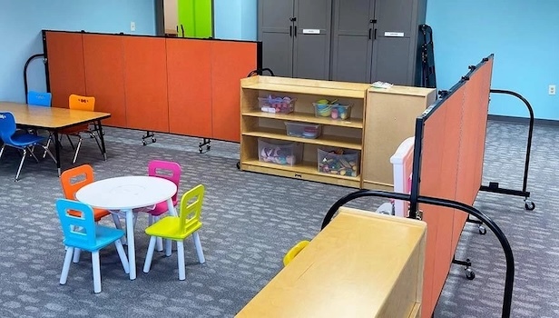 The importance of a healthy Sunday School program - How to increase Your Sunday School Attendance| Screenflex Room Dividers Orange portable room divider panels separating activity areas in a daycare classroom with colorful children's chairs, tables, and storage shelves.
