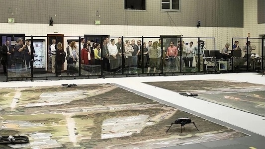 Spectators behind clear partitions during an indoor drone demonstration.