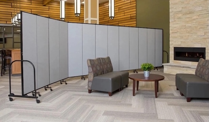 Freestanding gray room divider panels creating a temporary partition in a modern lounge area with chairs, a coffee table, and fireplace.