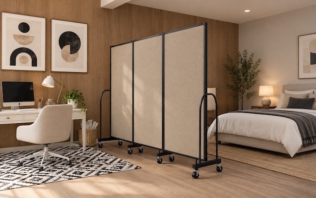 Beige portable room divider with black metal frame and caster wheels separating a home office workstation from a bedroom in a modern studio apartment.