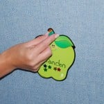 A woman's hand tacks a paper apple to a blue fabric tackable board