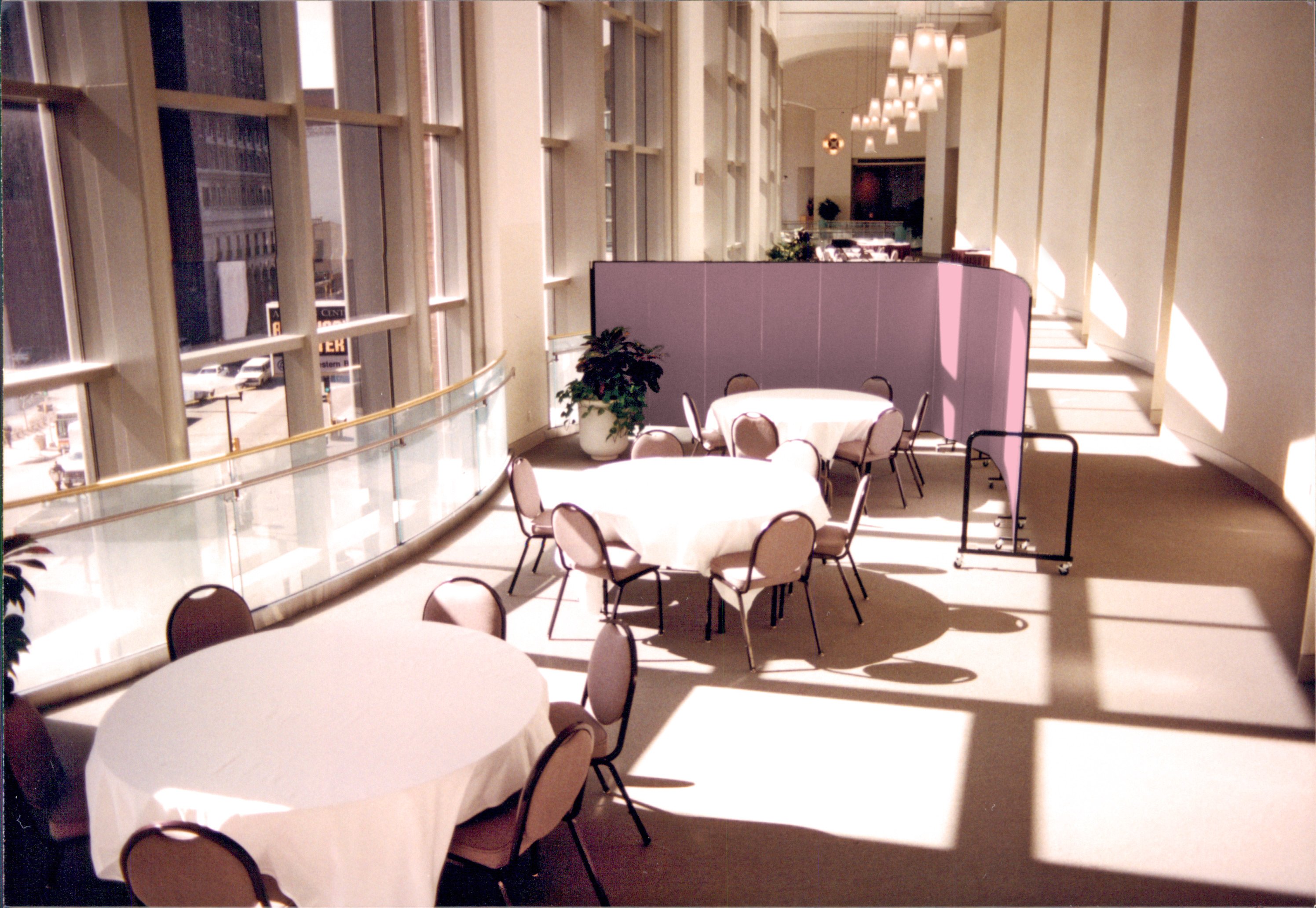 The sun shines onto three round banquet tables and chairs arranged in a banquet hall shielded on one side by a portable room divider