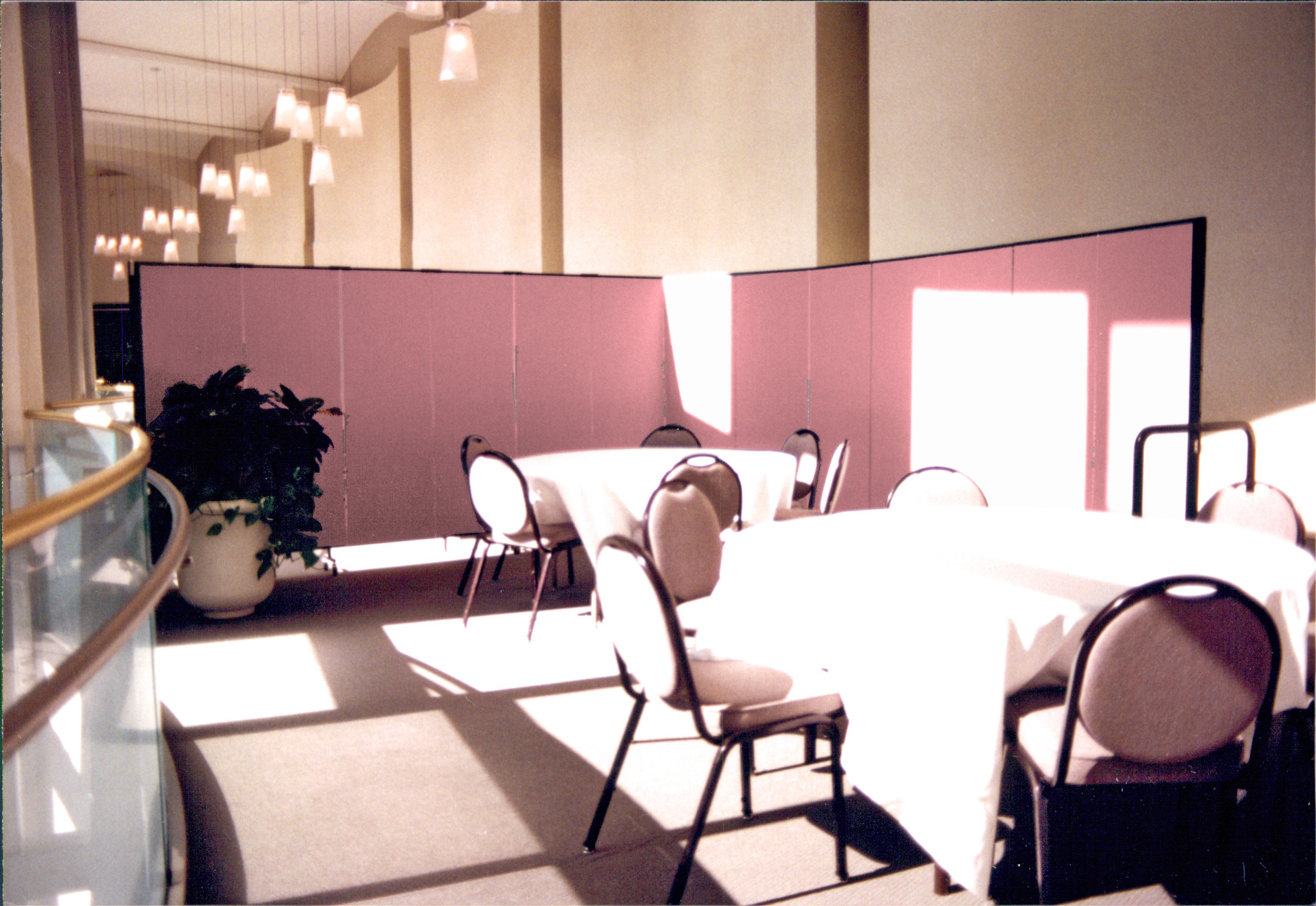 A set of round banquet tables and chairs arranged next to a set of windows and hidden from a hallway by a rolling room divider