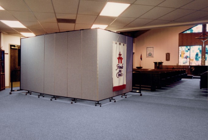 Situated behind rows of pews in a church, a blue room divider separates a room from the sanctuary