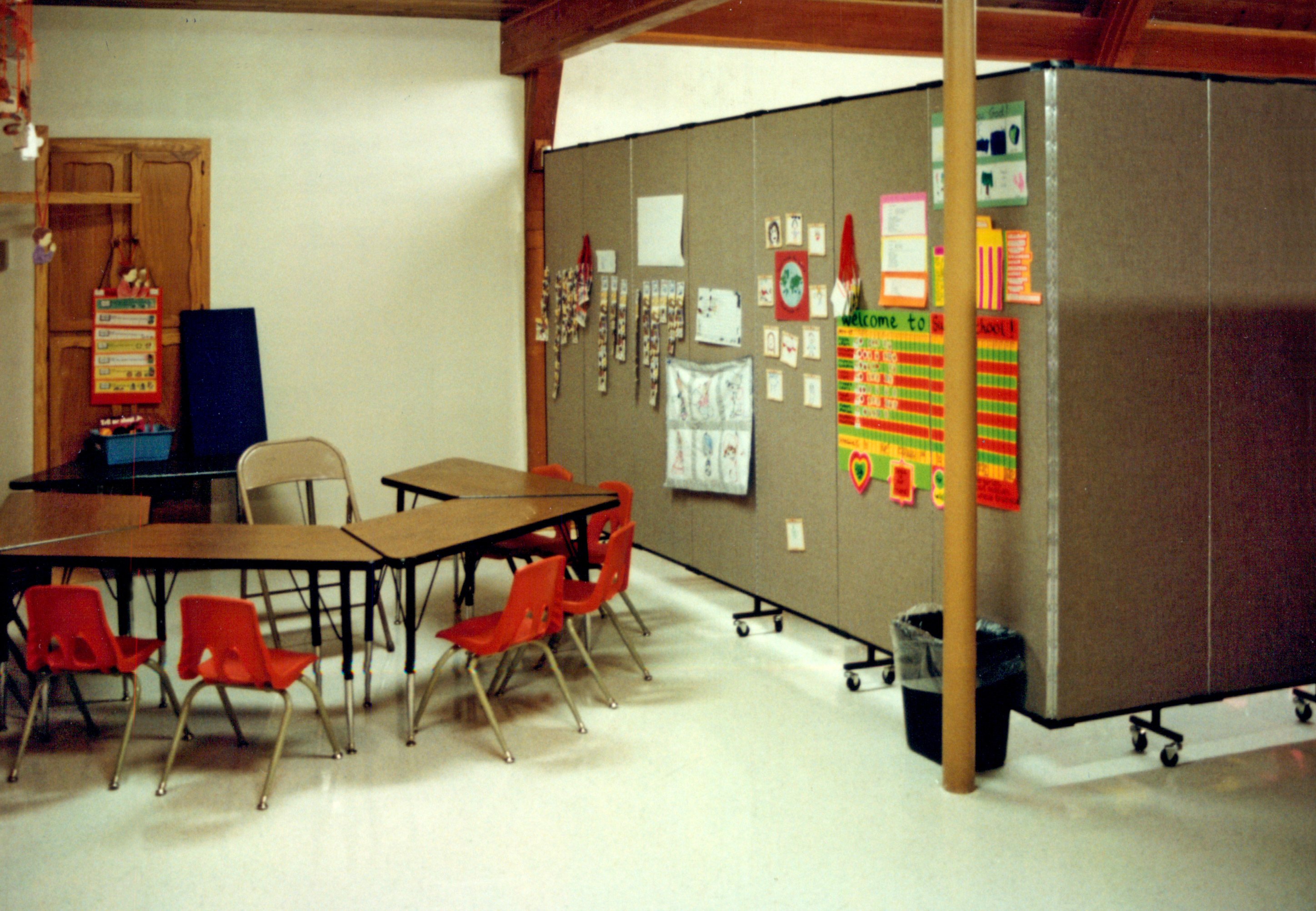 Student tables and chairs next to a room divider panel with educational material tacked to the fabric surface