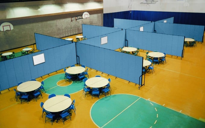 Several blue room dividers are used to divide round tables and chairs in each of the eight classrooms