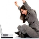 A woman sits on the floor looking at a computer celebrates with her arms up