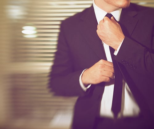 A man fixing his black tie while wearing a suit