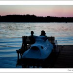 A couple sit on a bench on a pier looking over the water