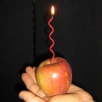 A lit squiggly candle stuck in an apple resting on the palm of a hand
