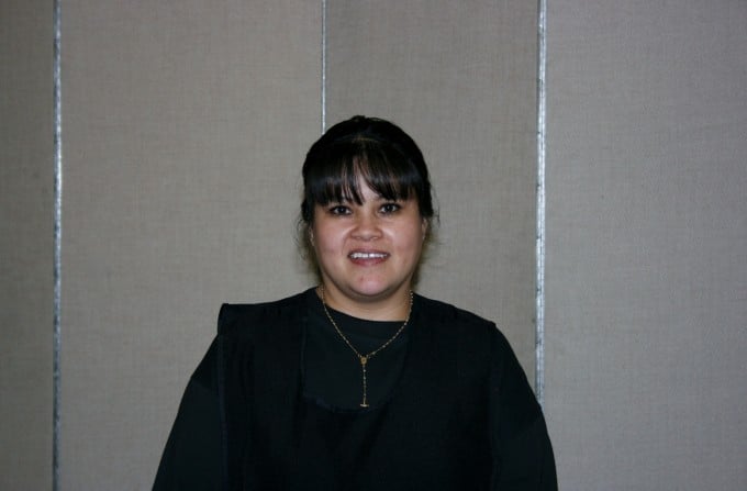 A woman with dark hair and dark clothes stands infront of a fabric wall 