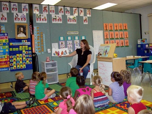 A room divider separates a room into two kindergarten classrooms filled with students and teachers