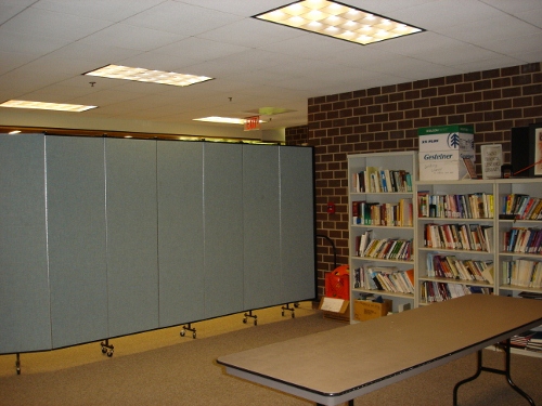 Book shelves line a brick wall next to a portable room divider wall