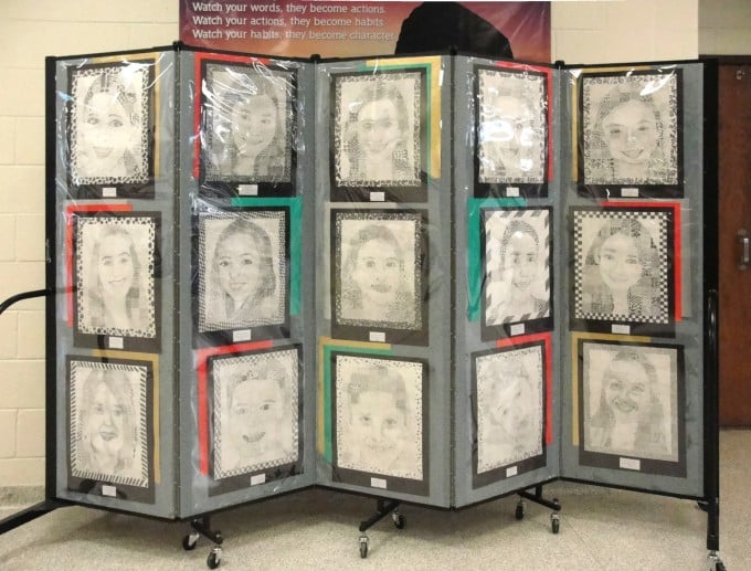 Student self portraits hang on a Screenflex Portable Partition