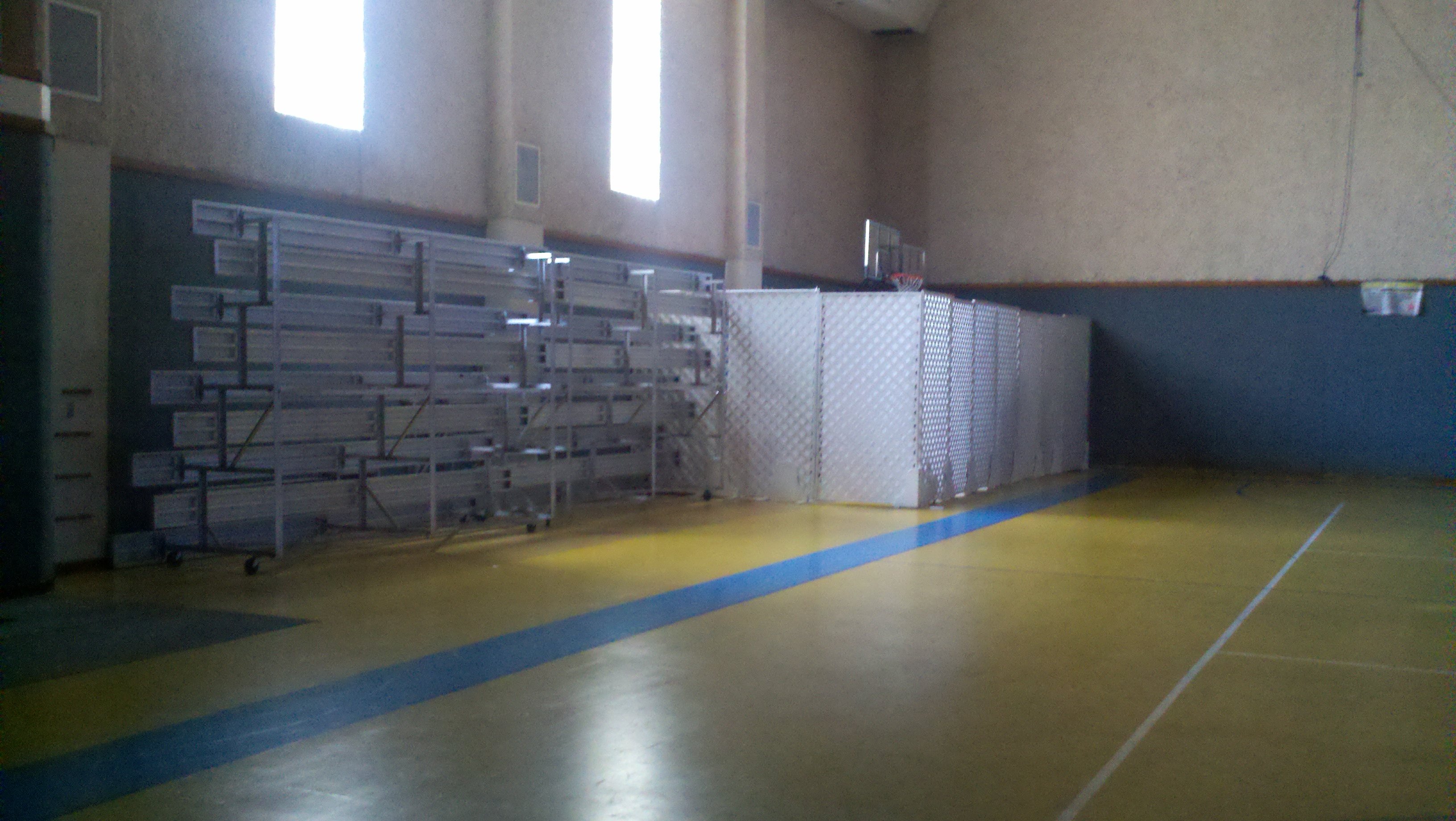 Metal bleachers folded against a wall next to fabric covered lattice shielding basketball equipment