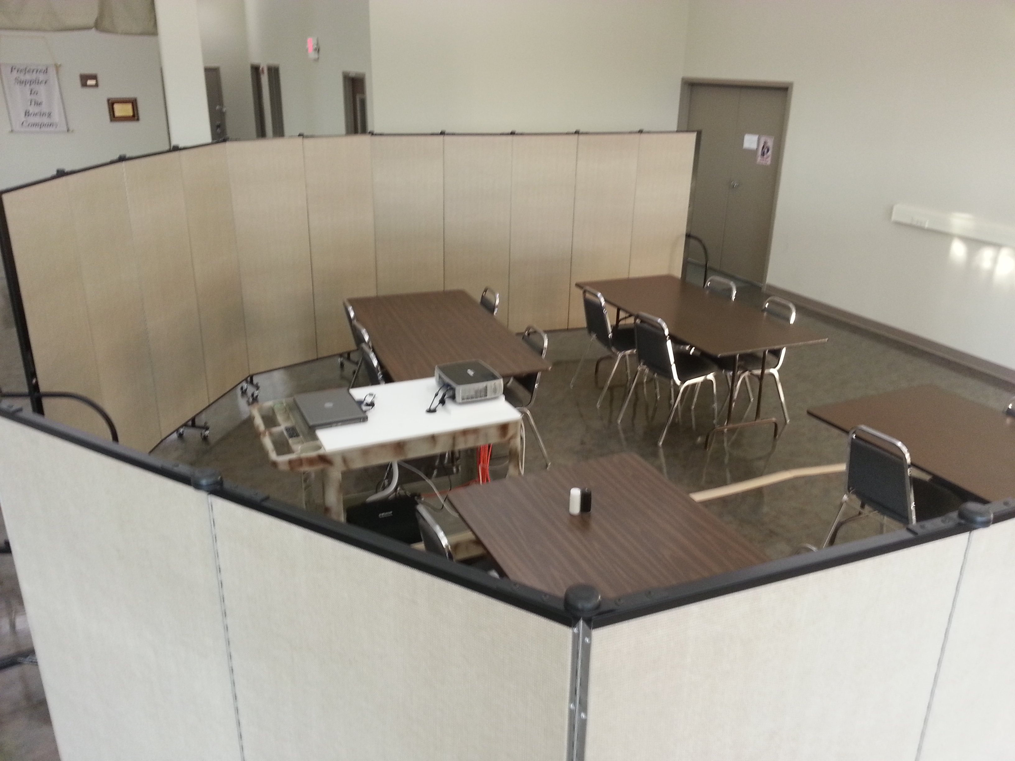 Screenflex Room Dividers are arranged around a group of 4 tables and a projector to create a conference room within a large open meeting area.
