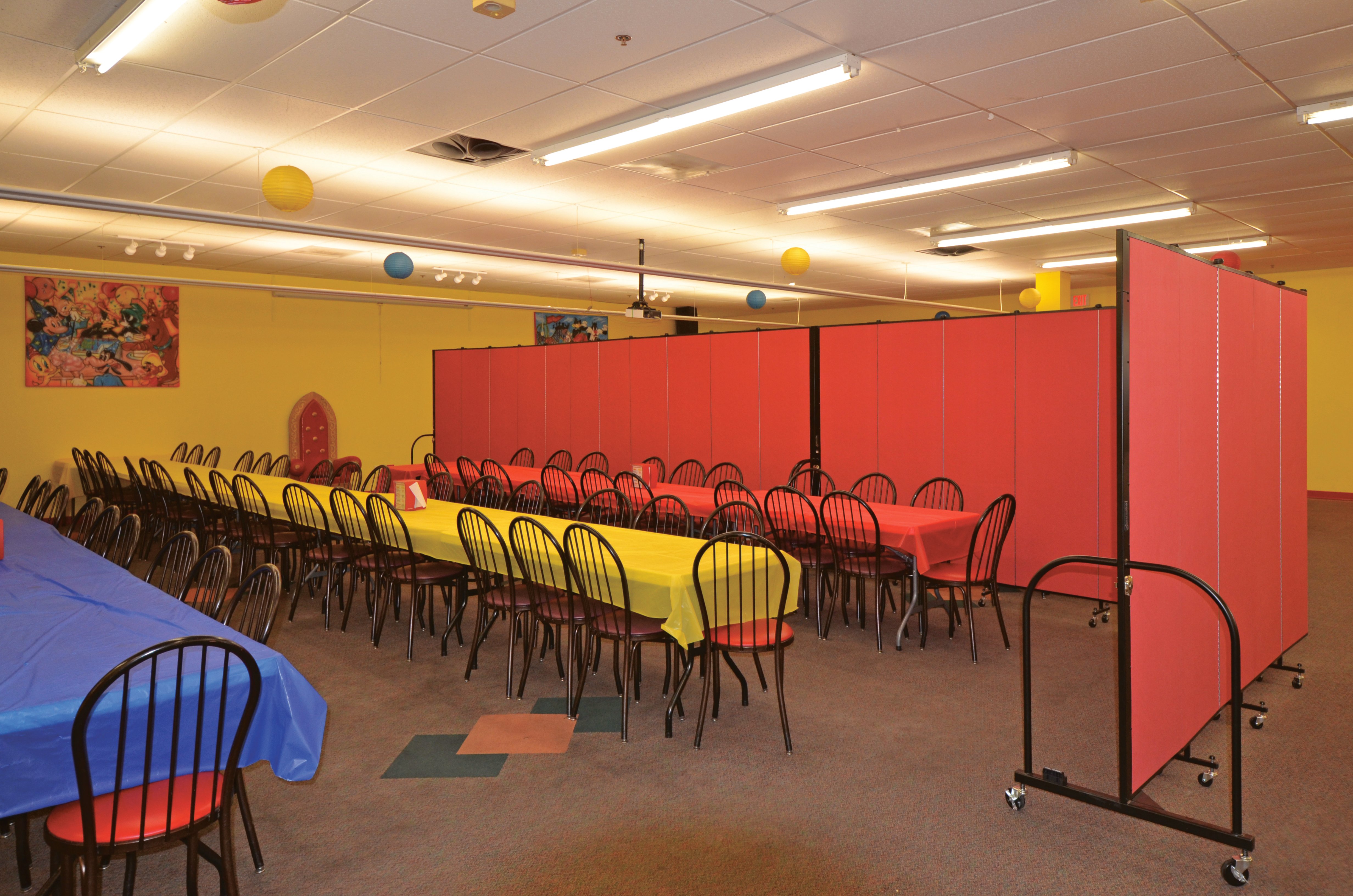 A colorful party room is divided into two eating areas with a red Screenflex Room Divider.