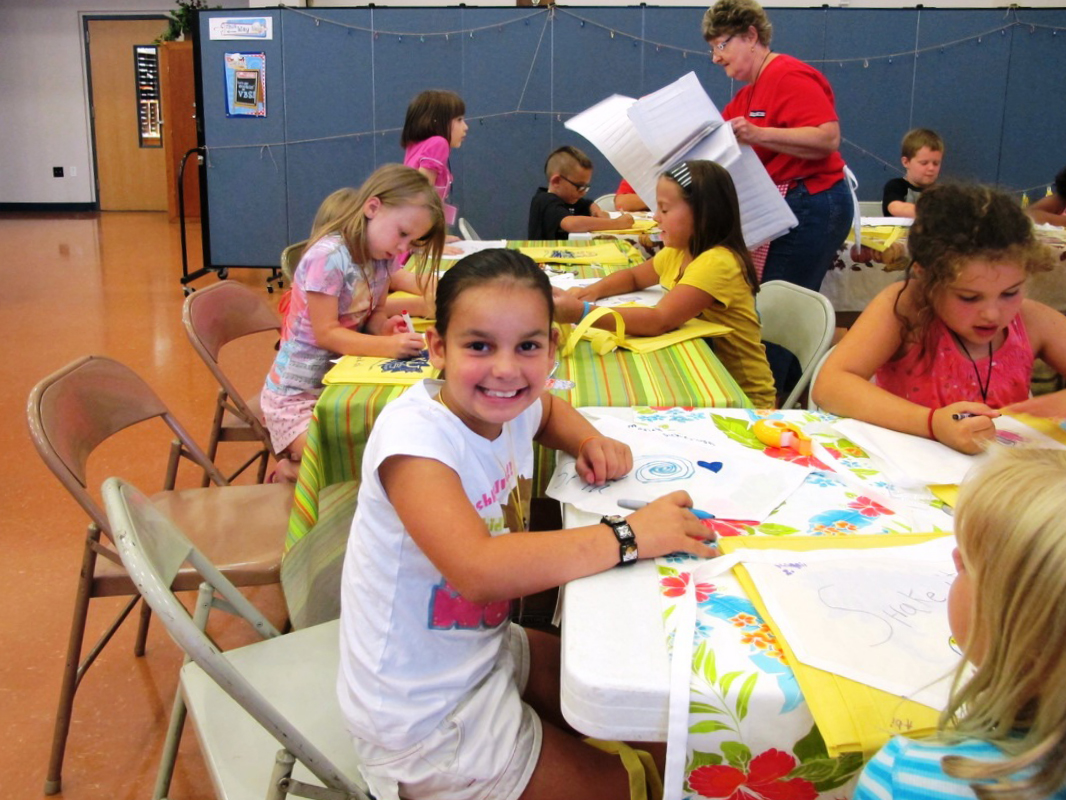 An elementary student stops coloring to pose for a picture during craft time at VBS.