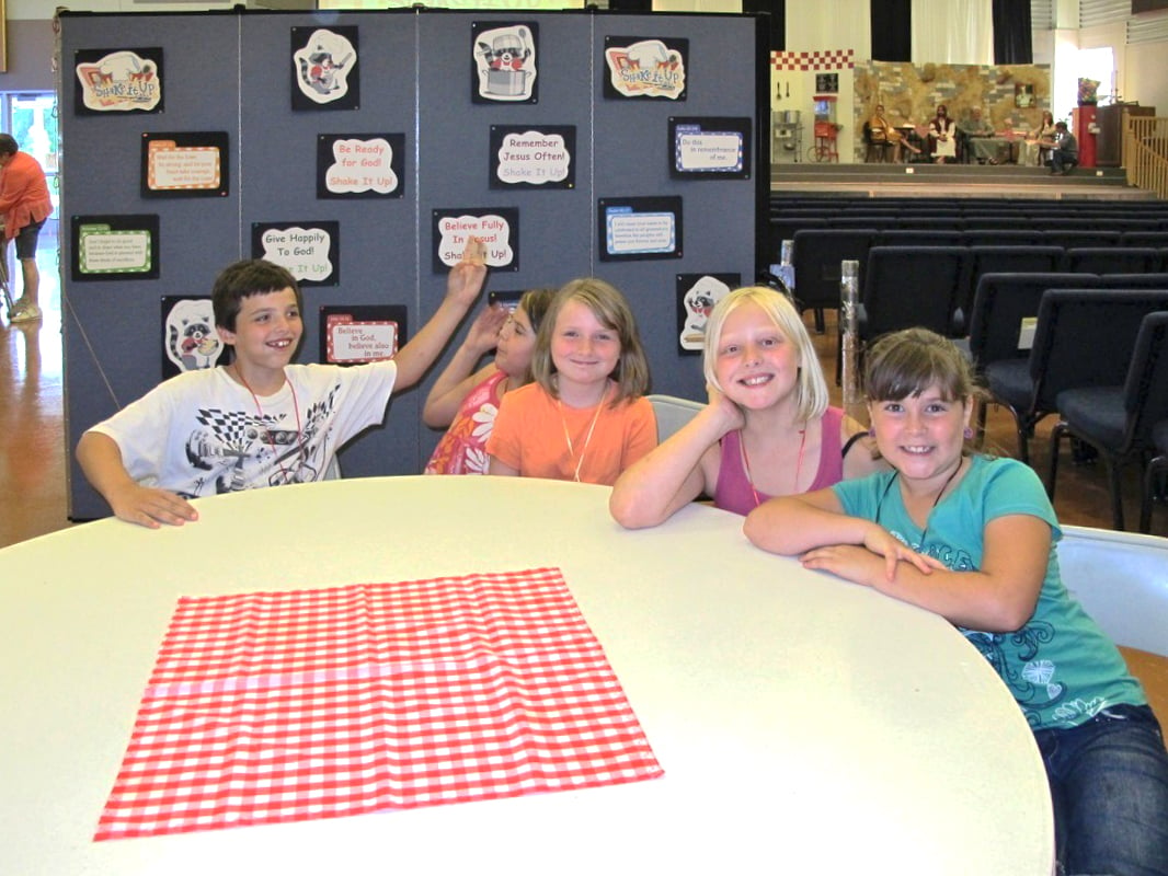 Students sit at a round table at a VBS camp help in a church sanctuary.