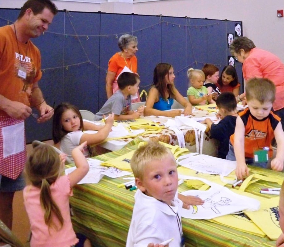 Male and Female adults helps young students color pictures during craft time at a VBS camp.