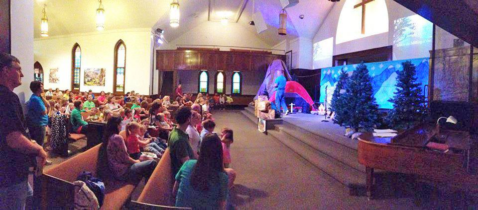 Families gather in a church to listen to a preacher speak from a stage decorated to look like a cold snowy night in the mountains.