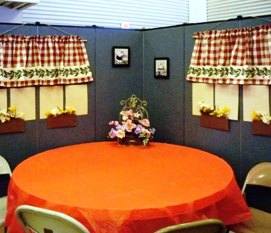 A round table covered in an orange table cloth sits at the center of room dividers decorated to resemble a restaurant.
