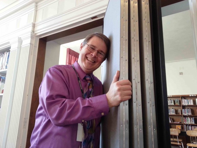 A man smiles and leans against a closed room partition