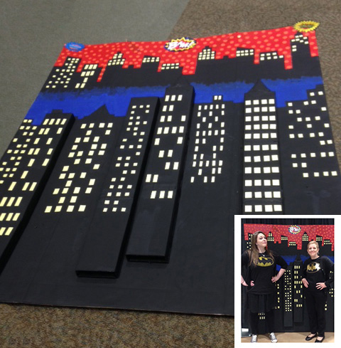 A comic con backdrop is created by using cardboard boxes. In the inset, a pair of superhero librarians pose in front of the painted prop