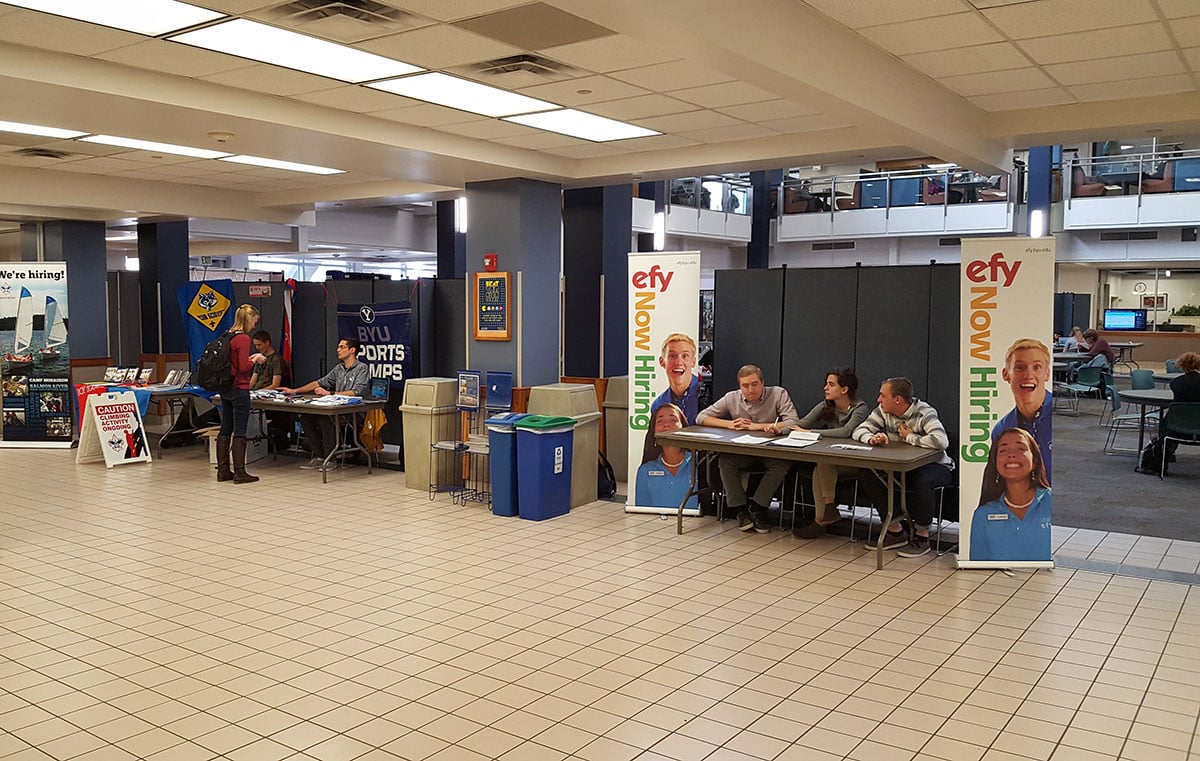 Display towers create a backdrop for employee recruiters sitting at tables in a hallway