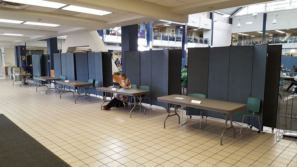 A female student sits at a long table in a hallway with blue display towers behind her