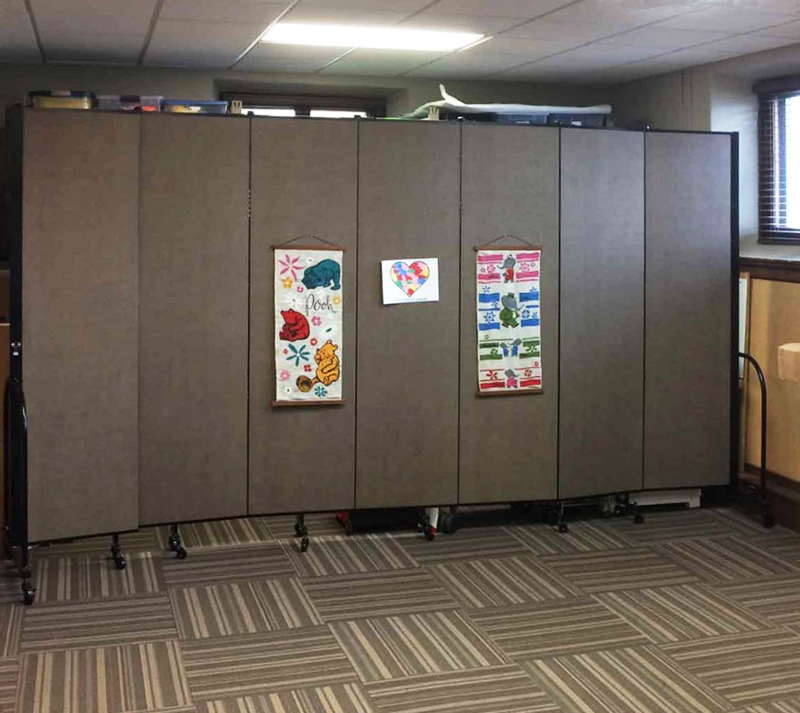 Posters are tacked to a 7-panel Screenflex folding wall partition that is opened in a classroom