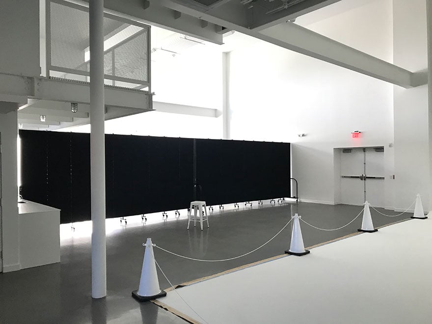 Large open white room is divided into two rooms by a set of black movable wall partitions