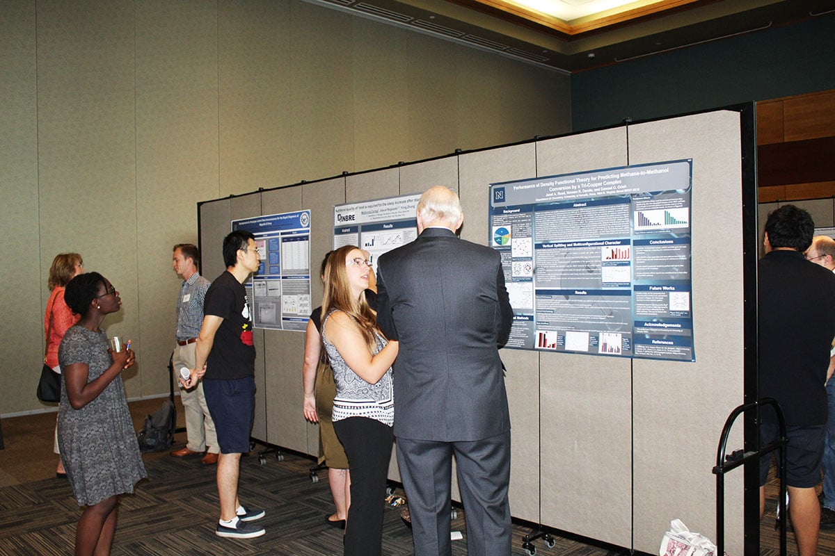 A man and woman review a college poster presentation tacked to a display wall
