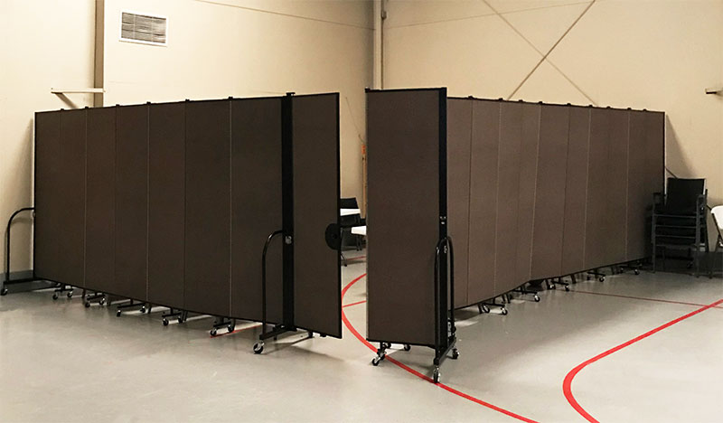 A set of brown accordion walls form a square room in the corner of a gym