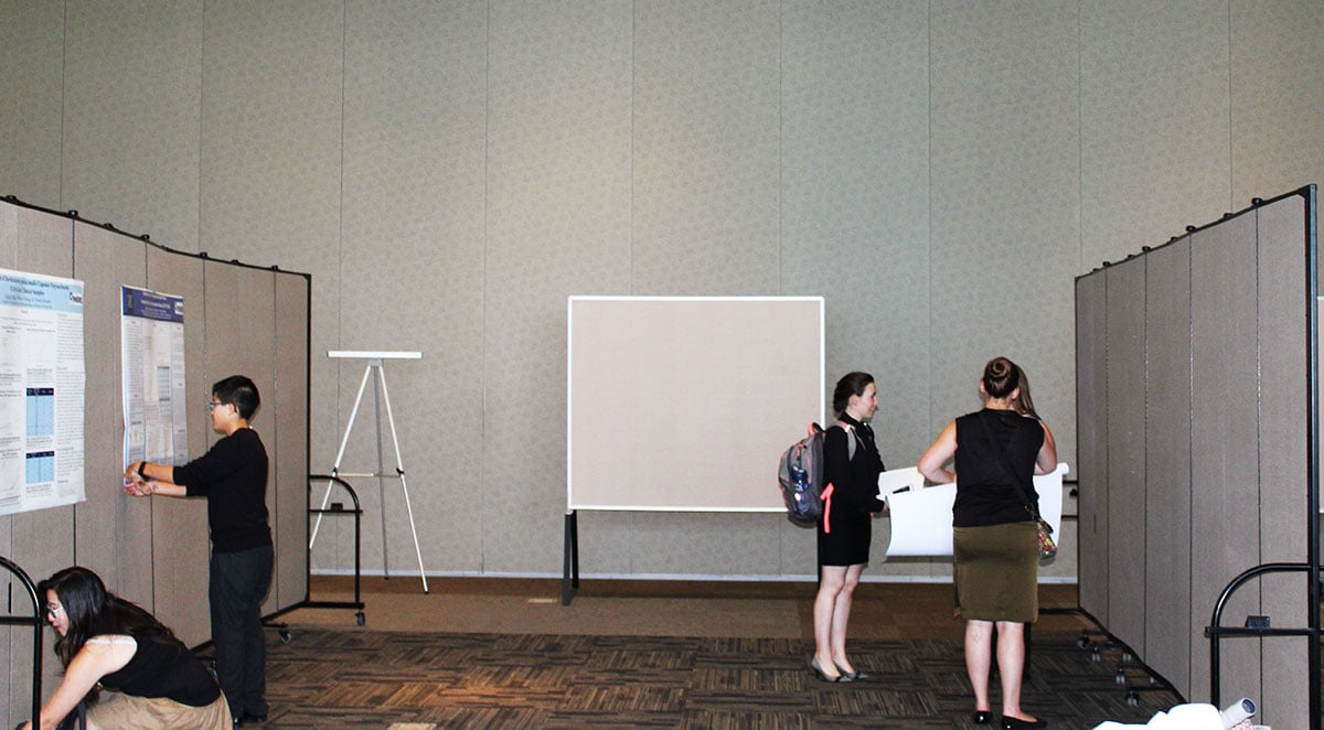 Students tack college research posters to a set of movable bulletin boards