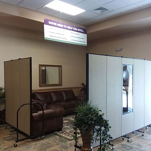 A set of room dividers with windows surround a pair of couches to create a church welcome center