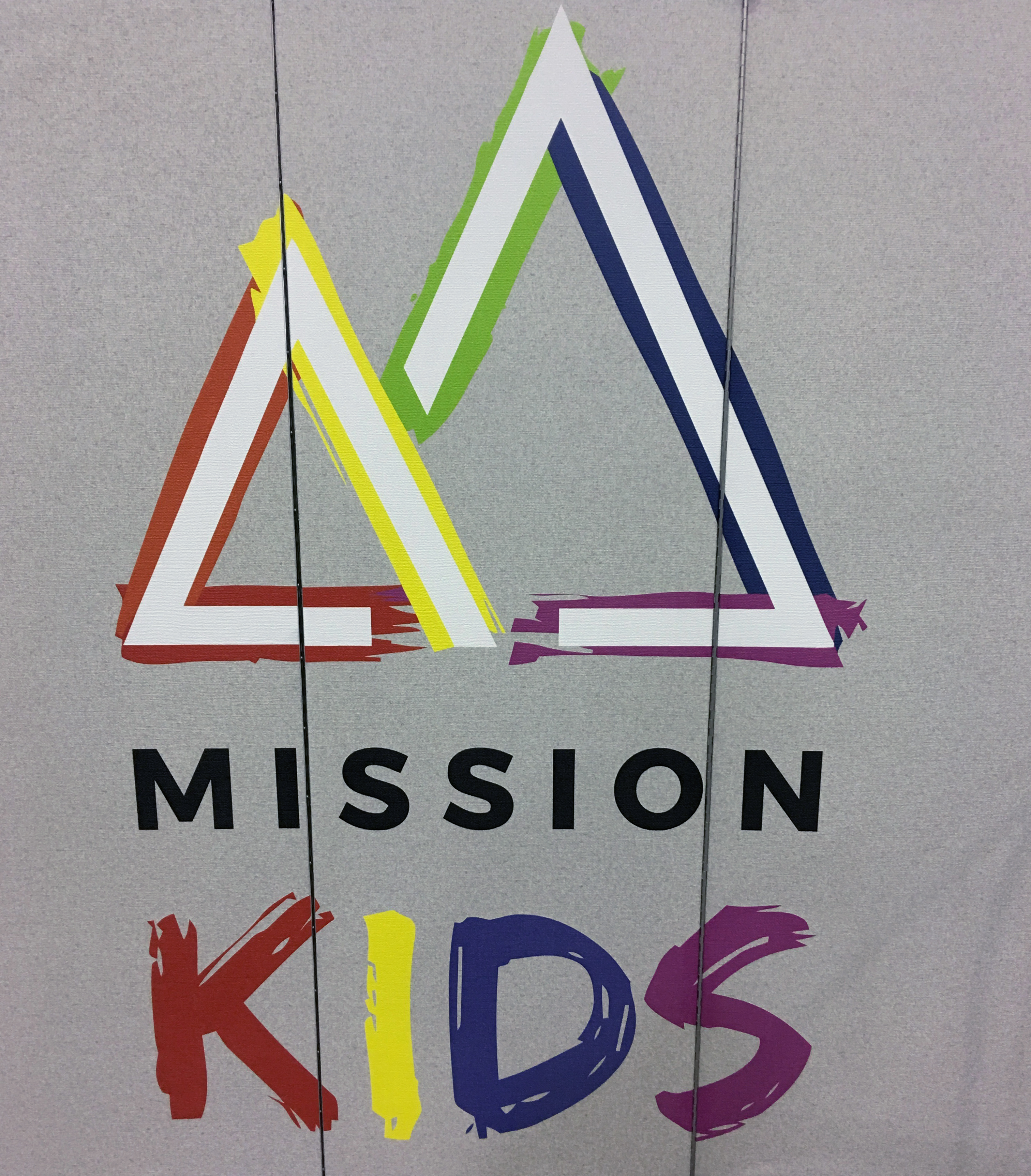 Colorful Mission Kids logo on a grey room divider