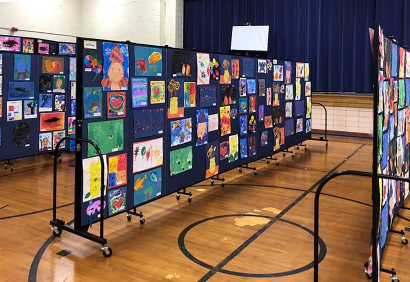 Three portable art display walls display artwork in a school gym