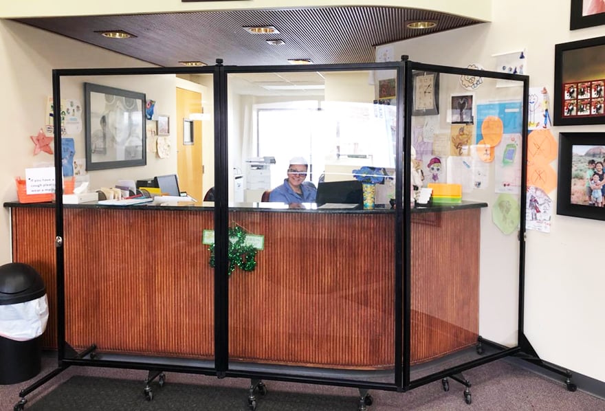 clear medical barrier in front of brown check-in desk and receptionist