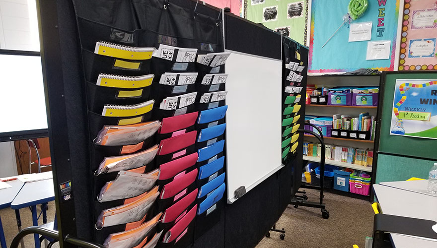 black room divider in a classroom with folders and whiteboard hanging from it