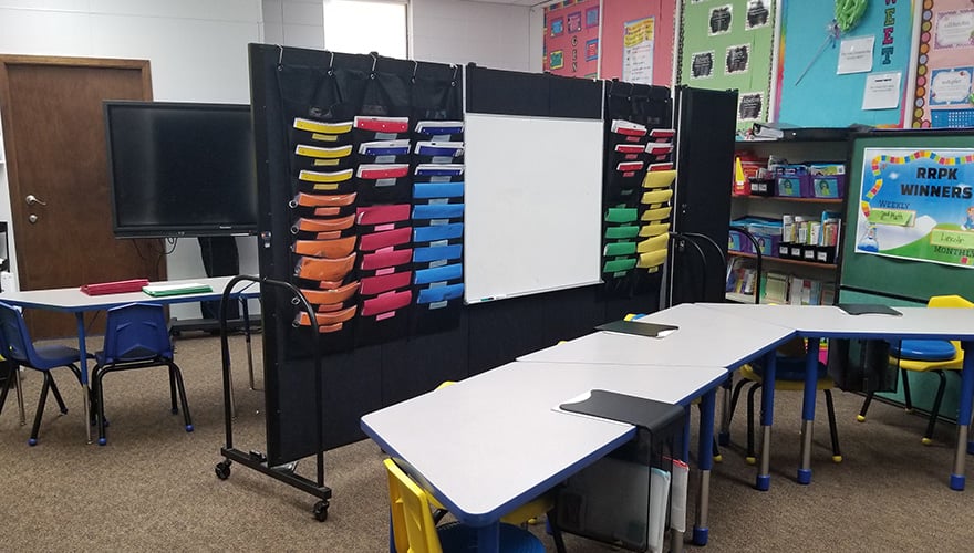 black room divider in a classroom with folders and whiteboard hanging from it