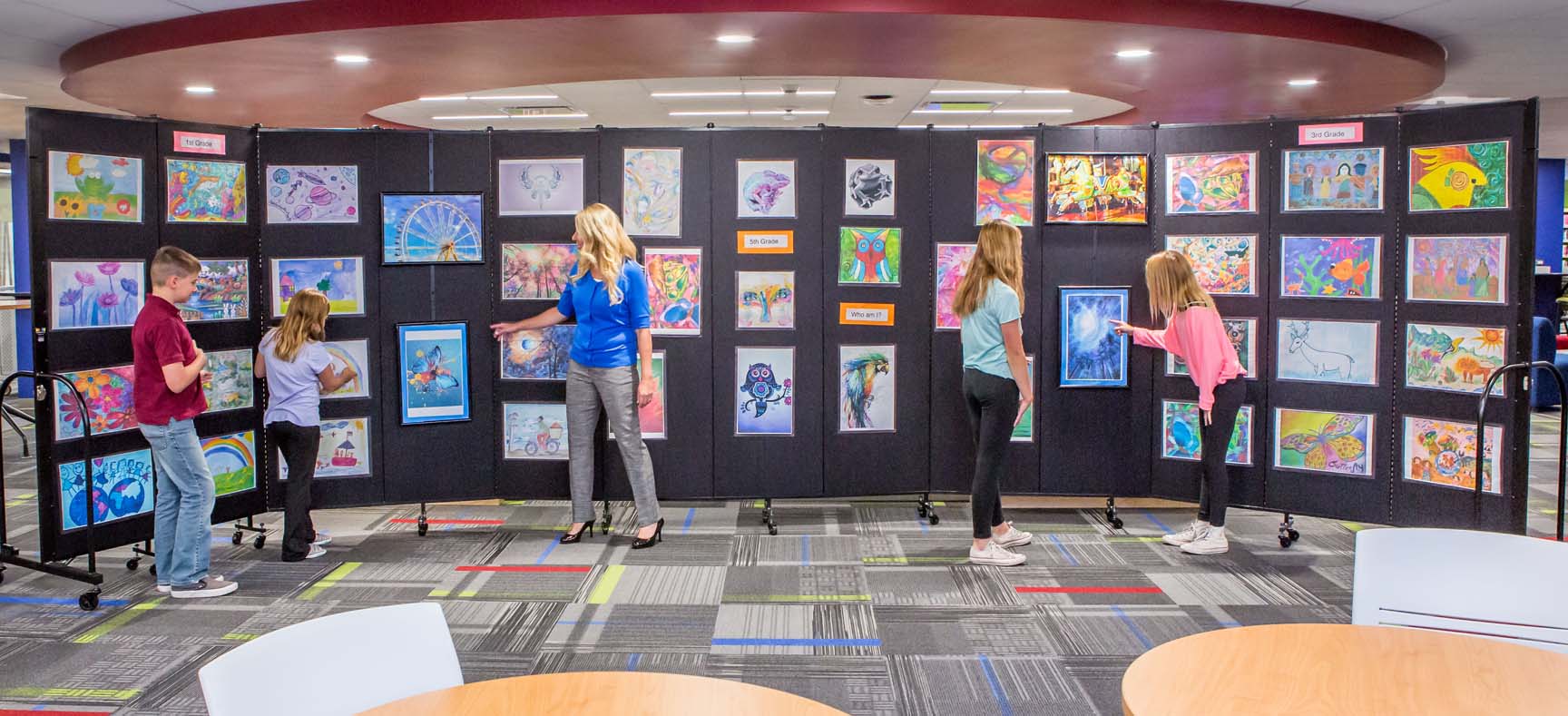 four kids and one woman standing in front of an art display and looking at pictures