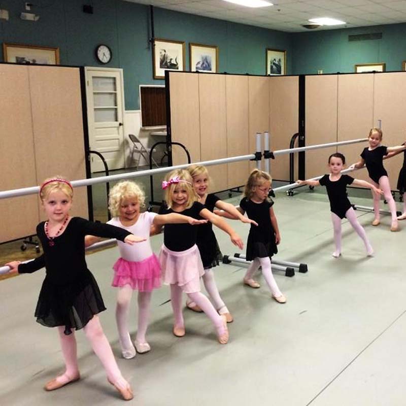 little kids doing ballet poses on a barre in front of tan dividers