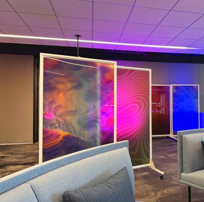 Colorful abstract panels on rolling frames in a modern lounge, with pink lighting and upholstered seating in the foreground.